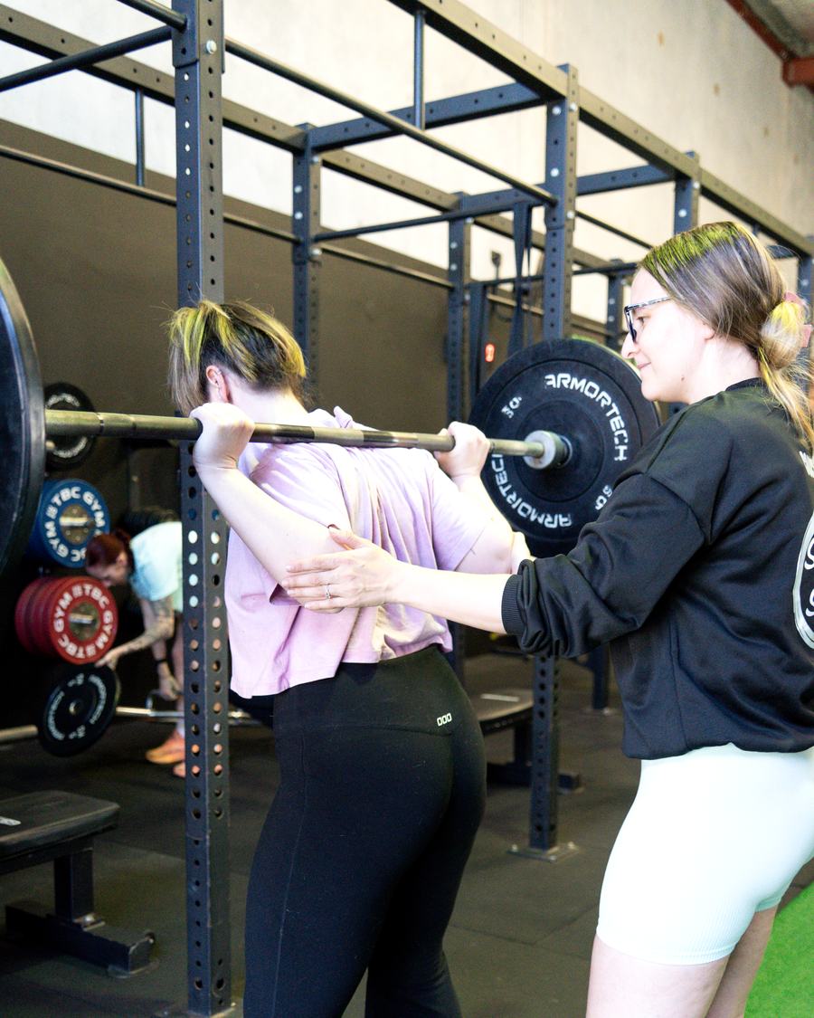 Maddie coaching a member through a barbell squat
