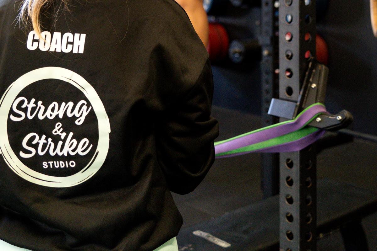 A Strong and Strike Studio coach jacket on the gym floor beside the rack